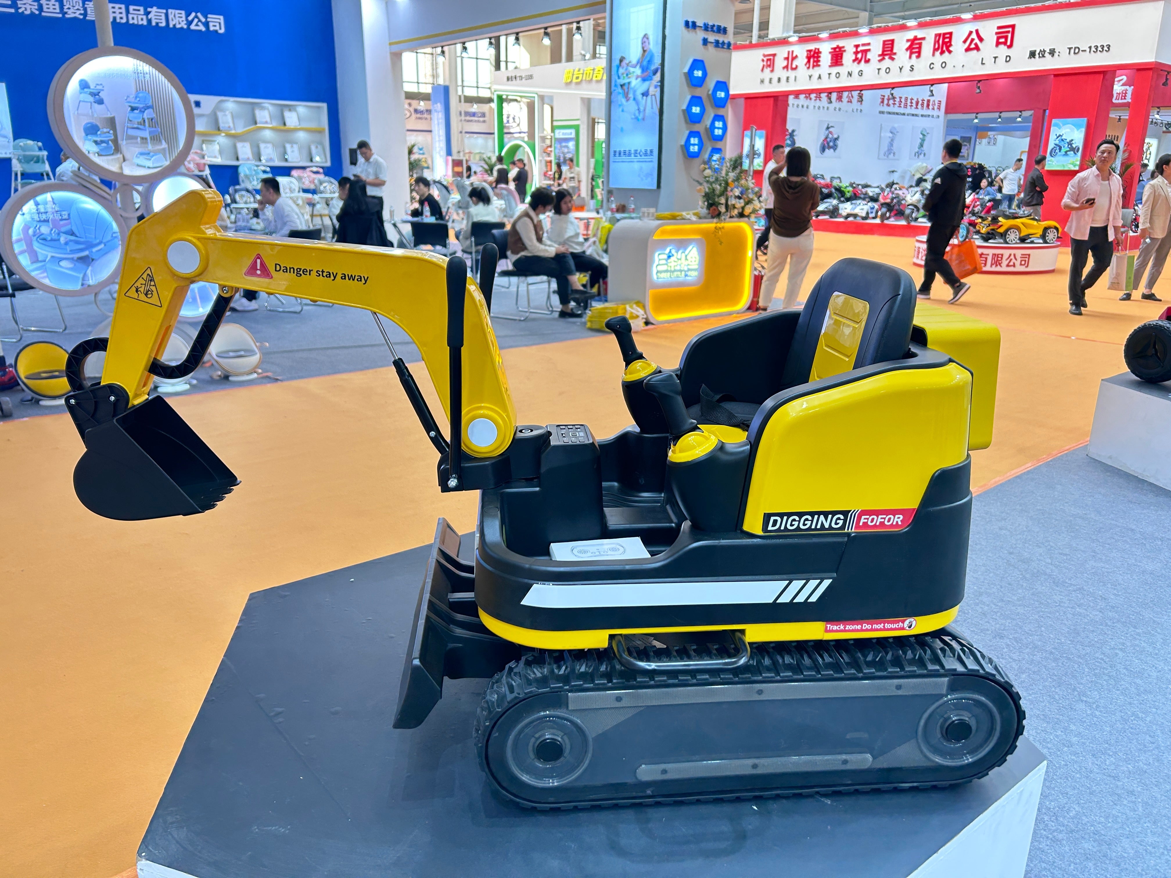 Yellow 24V kids ride-on excavator digger with manual arm, dual motors, and realistic controls on display indoors