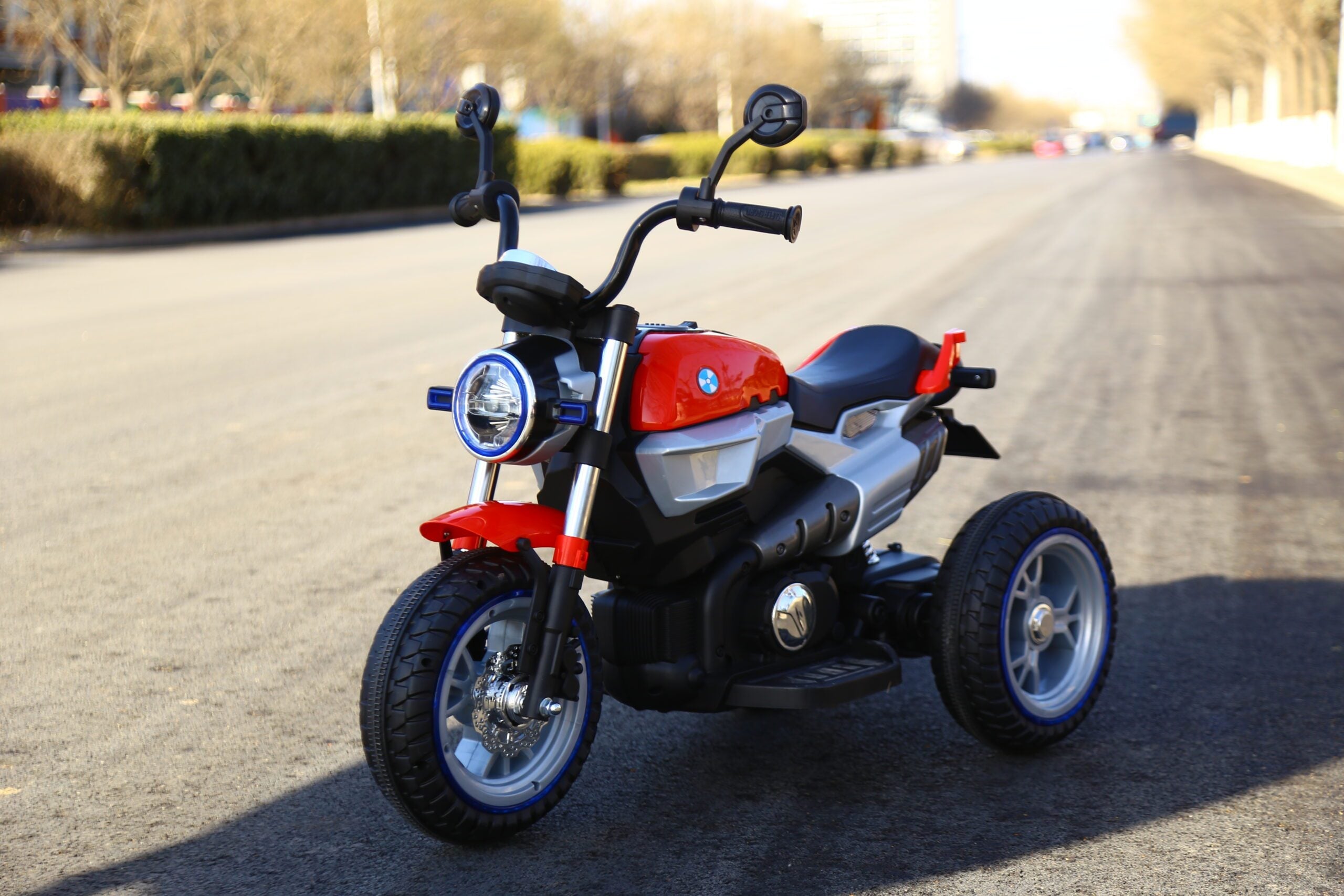 Red 12V kids electric ride-on motorcycle with lights and three wheels on a paved road outdoors