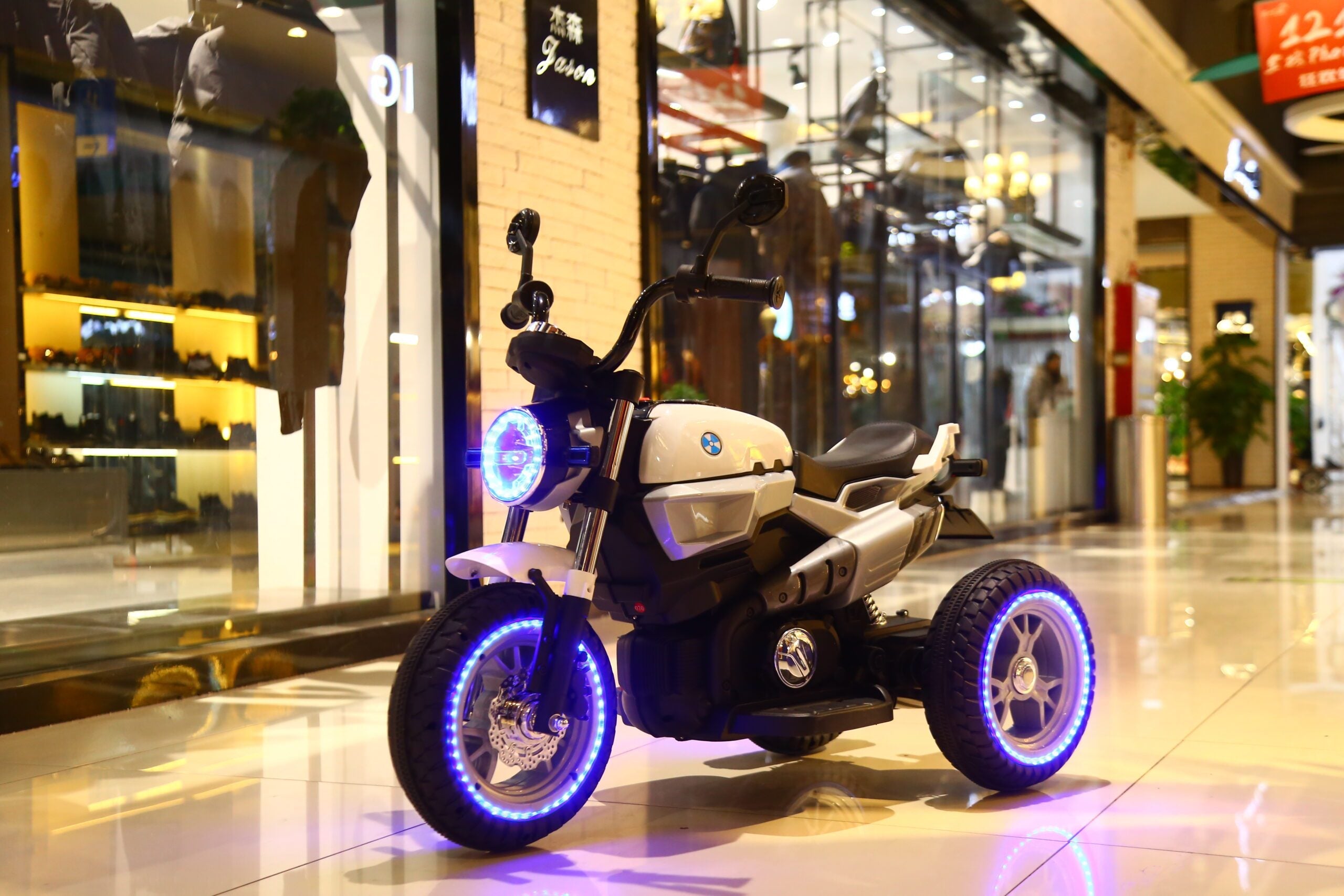 White kids electric ride-on motorcycle with blue LED lights on wheels and headlight in indoor setting