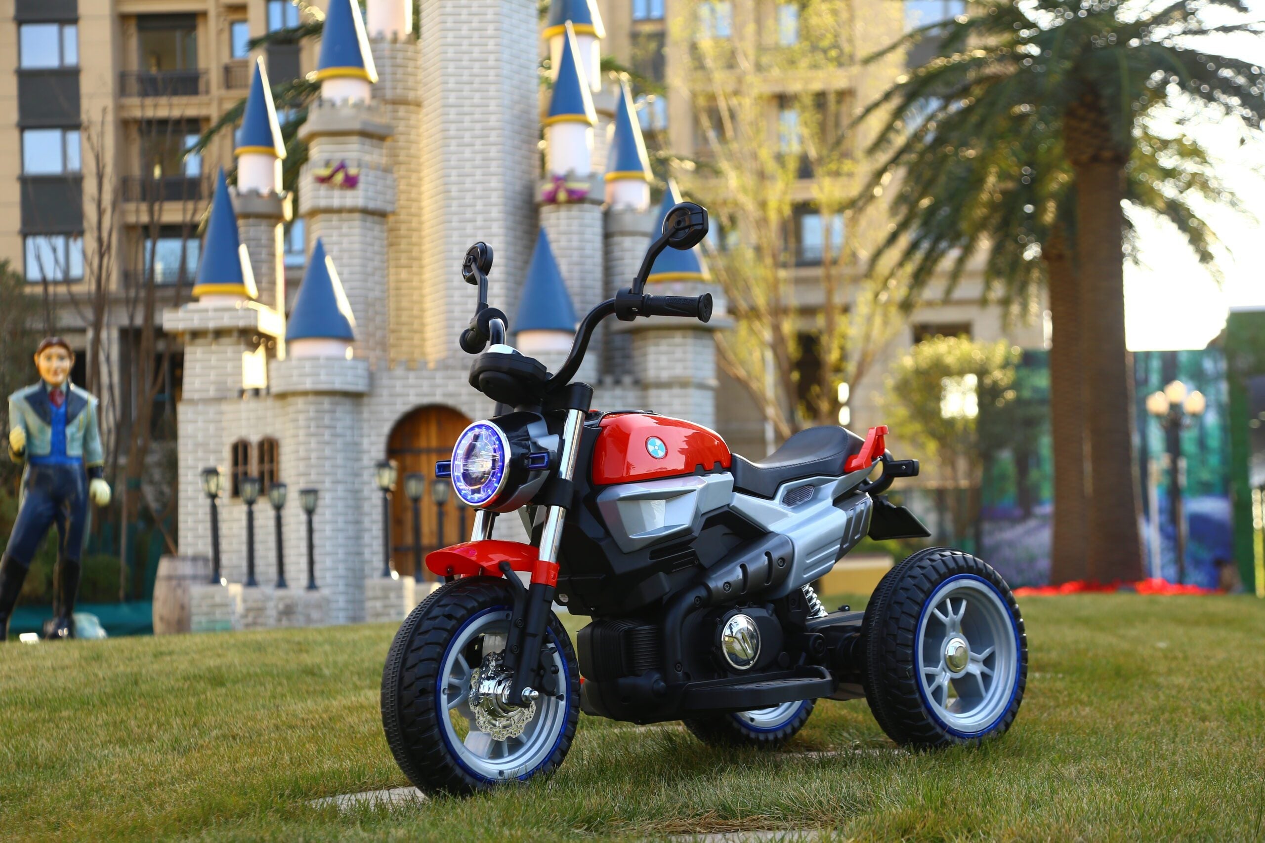 Red 12V kids ride-on electric motorcycle with LED lights, designed for ages 3 to 7, parked on grass outdoors.