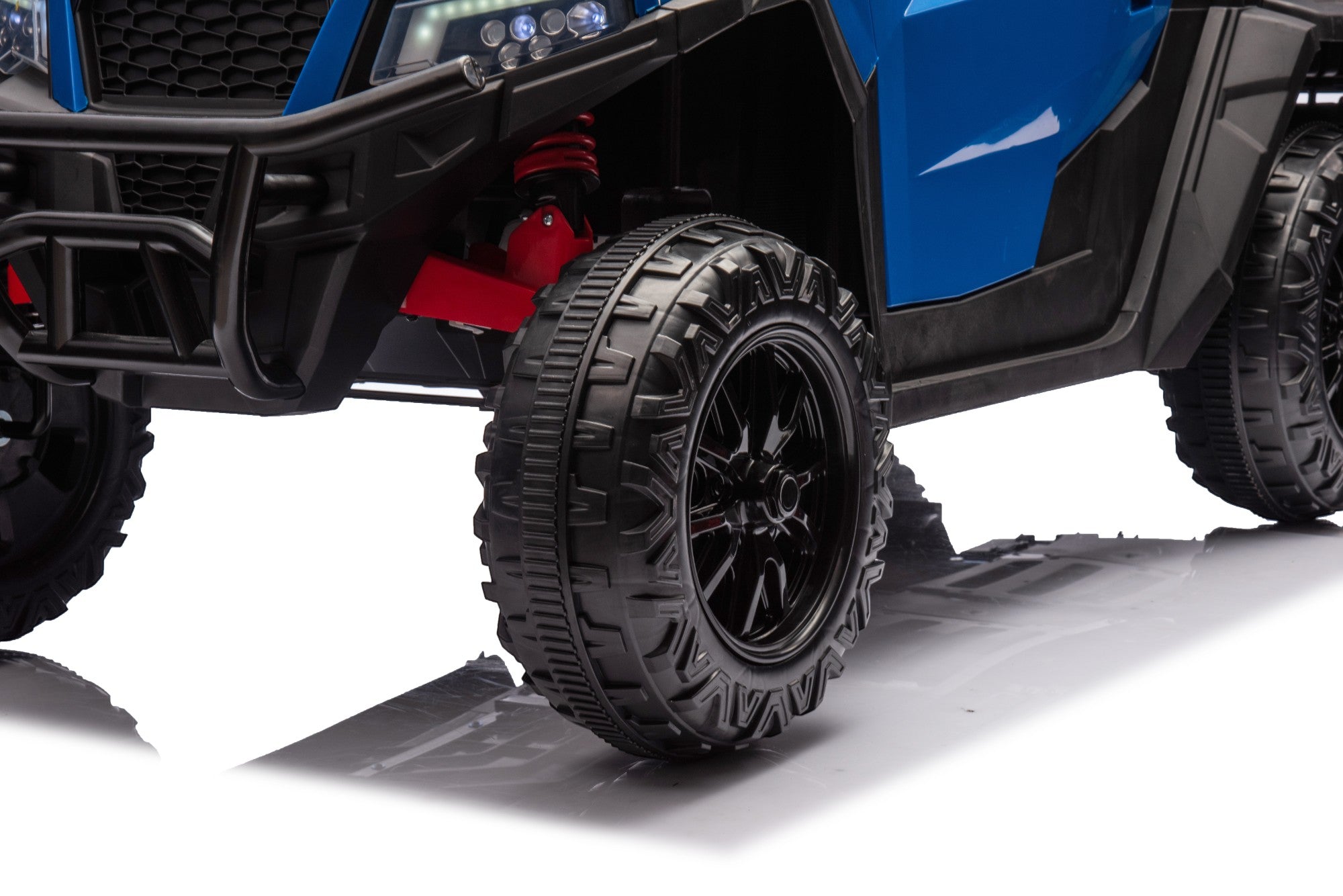 Close-up of the MC Wholesalers 24V Blue Kids Ride-On Dump Truck – 6-Wheel Electric Tipper, showcasing its large rugged black tire with deep treads, black rim, and red suspension in front against a white background.