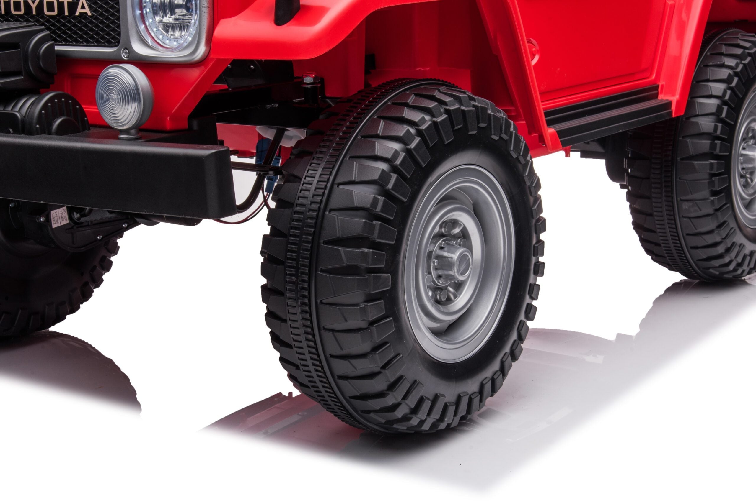 Close-up of black rugged tire and front part of red Toyota FJ40 LandCruiser 24V kids ride-on SUV
