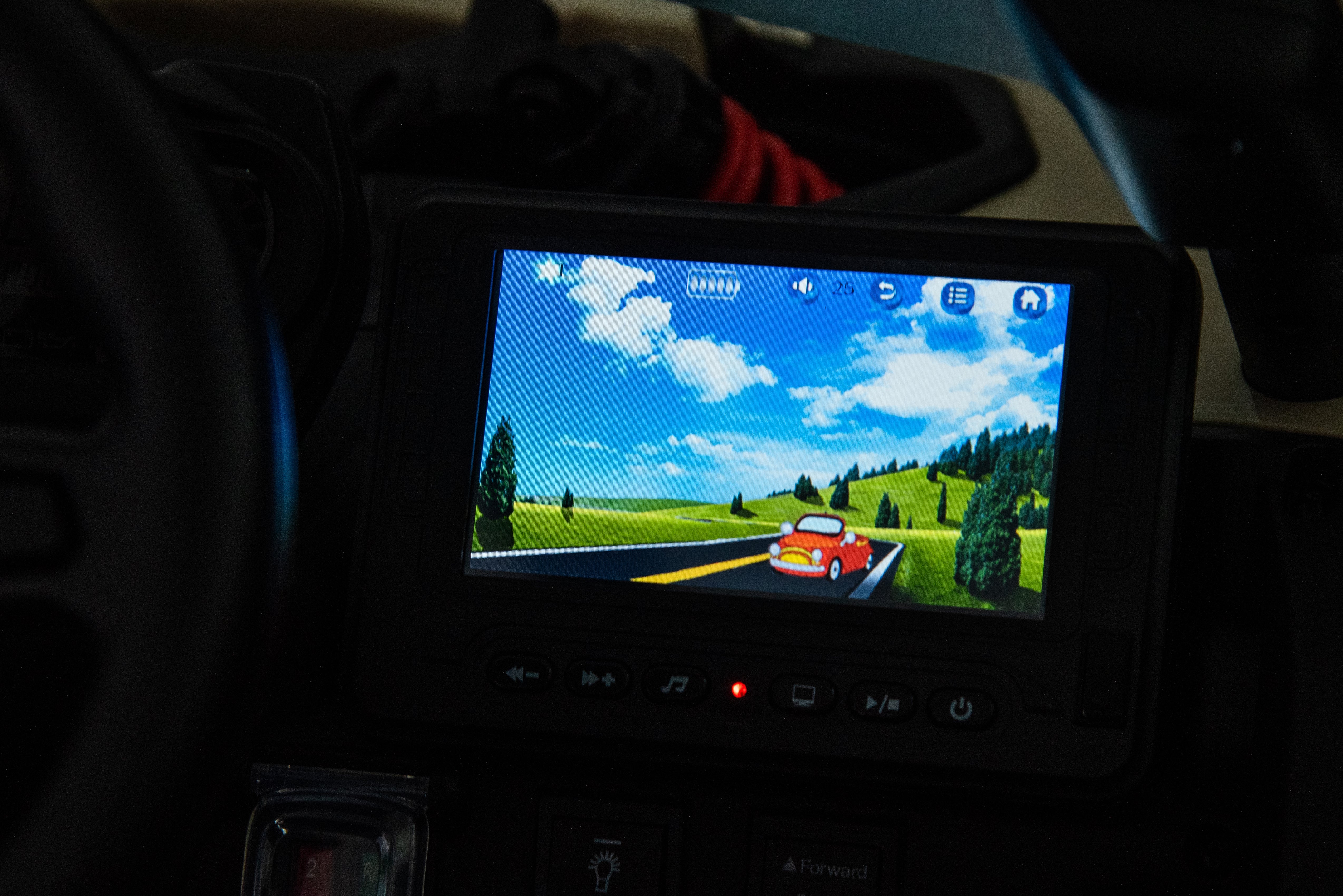 In-car entertainment screen displaying a colorful driving game with a red car on a scenic road background