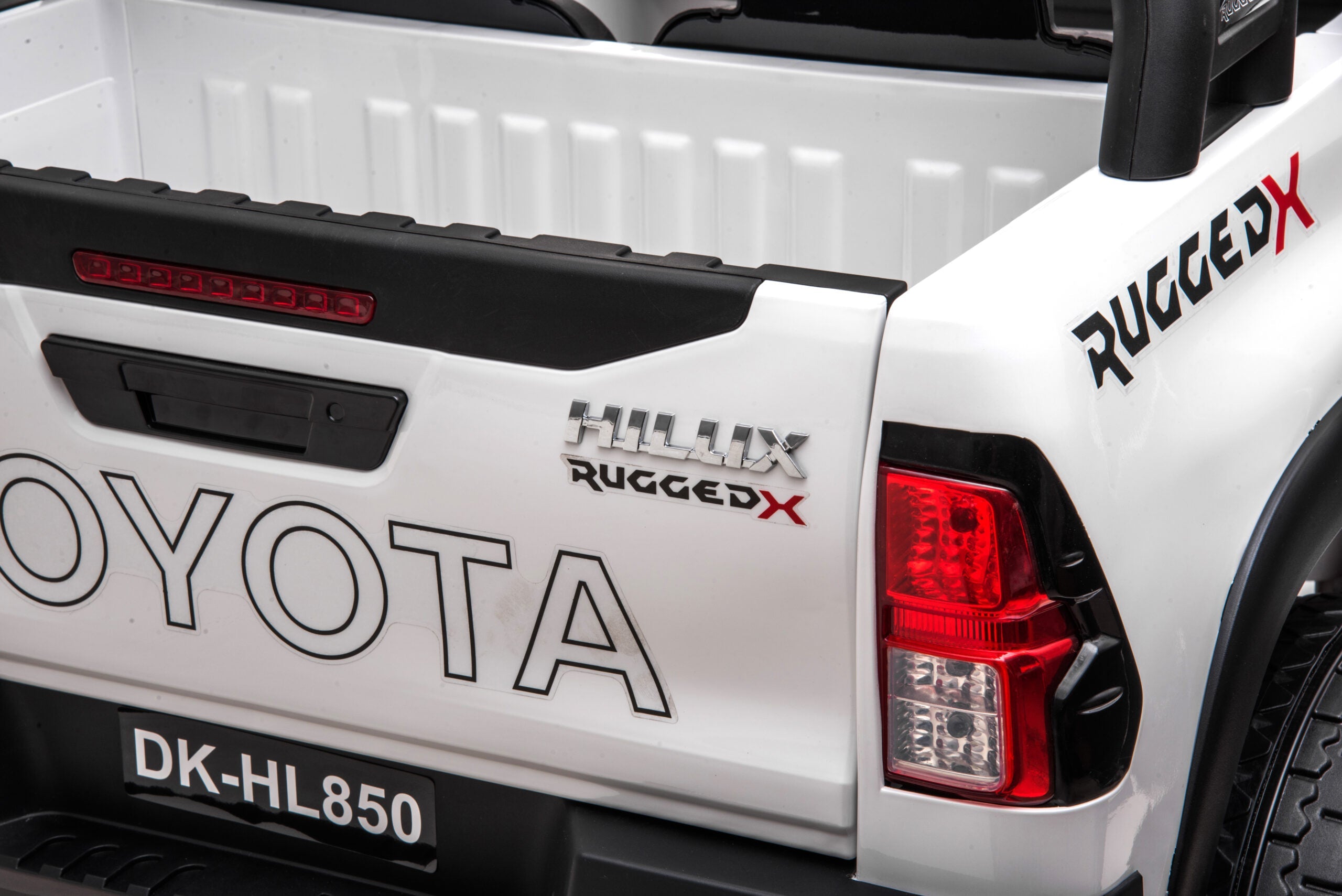 Close-up of the rear side of a white Licensed Toyota Hilux Rugged 24V kids ride-on car with taillight and rugged branding.