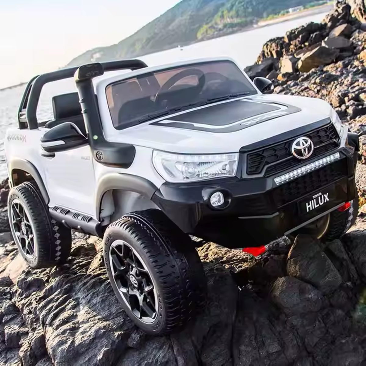 White Licensed Toyota Hilux Rugged 24V Kids Ride-On Car on rocky terrain with off-road tires and realistic details