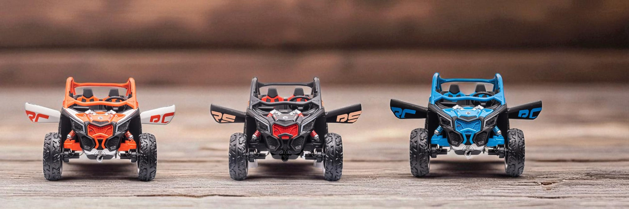 Three colorful small off-road toy vehicles lined up side by side on a wooden surface with a blurred background.