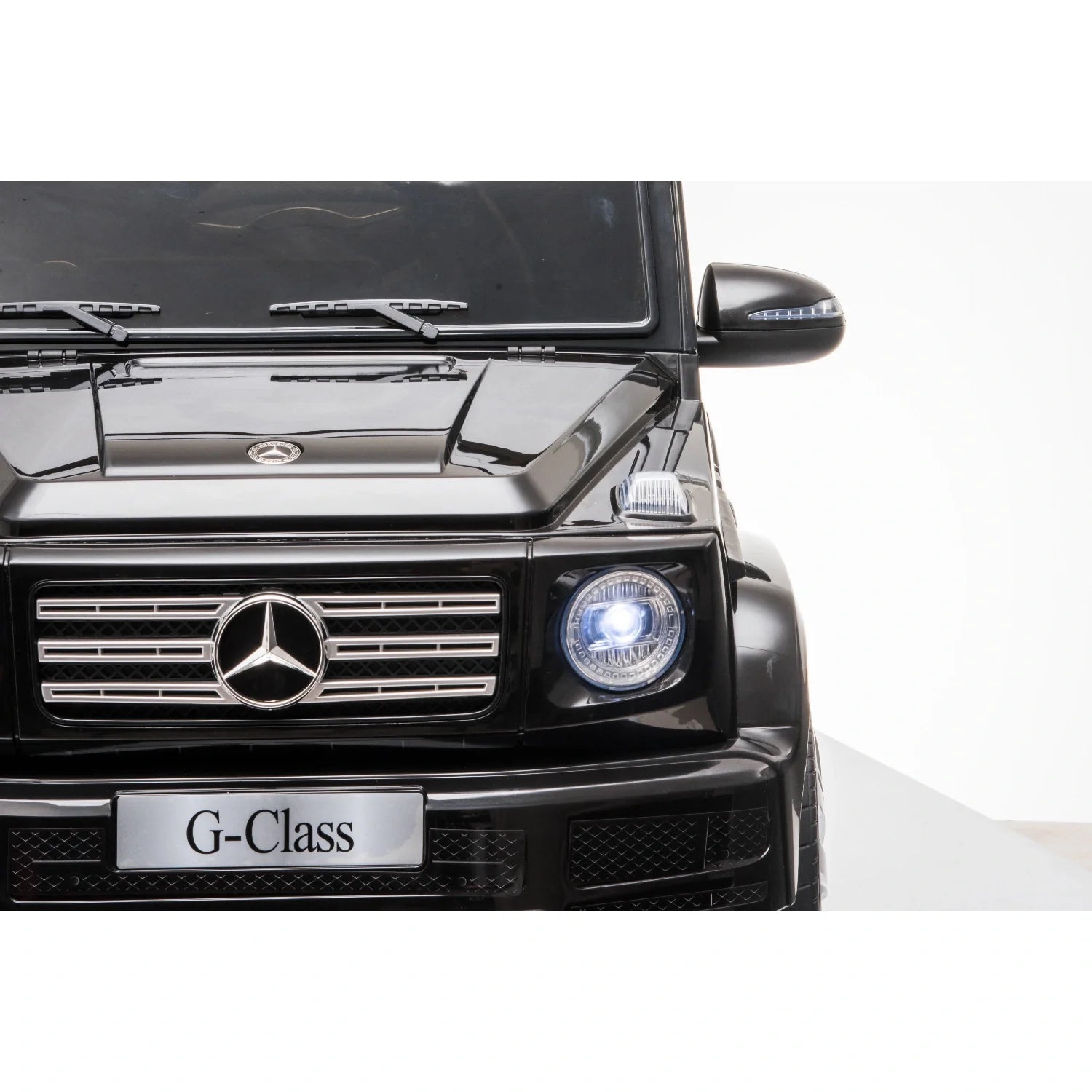 Front view of black 12V licensed Mercedes G-Wagon G63 kids electric ride-on car with headlight on and G-Class plate