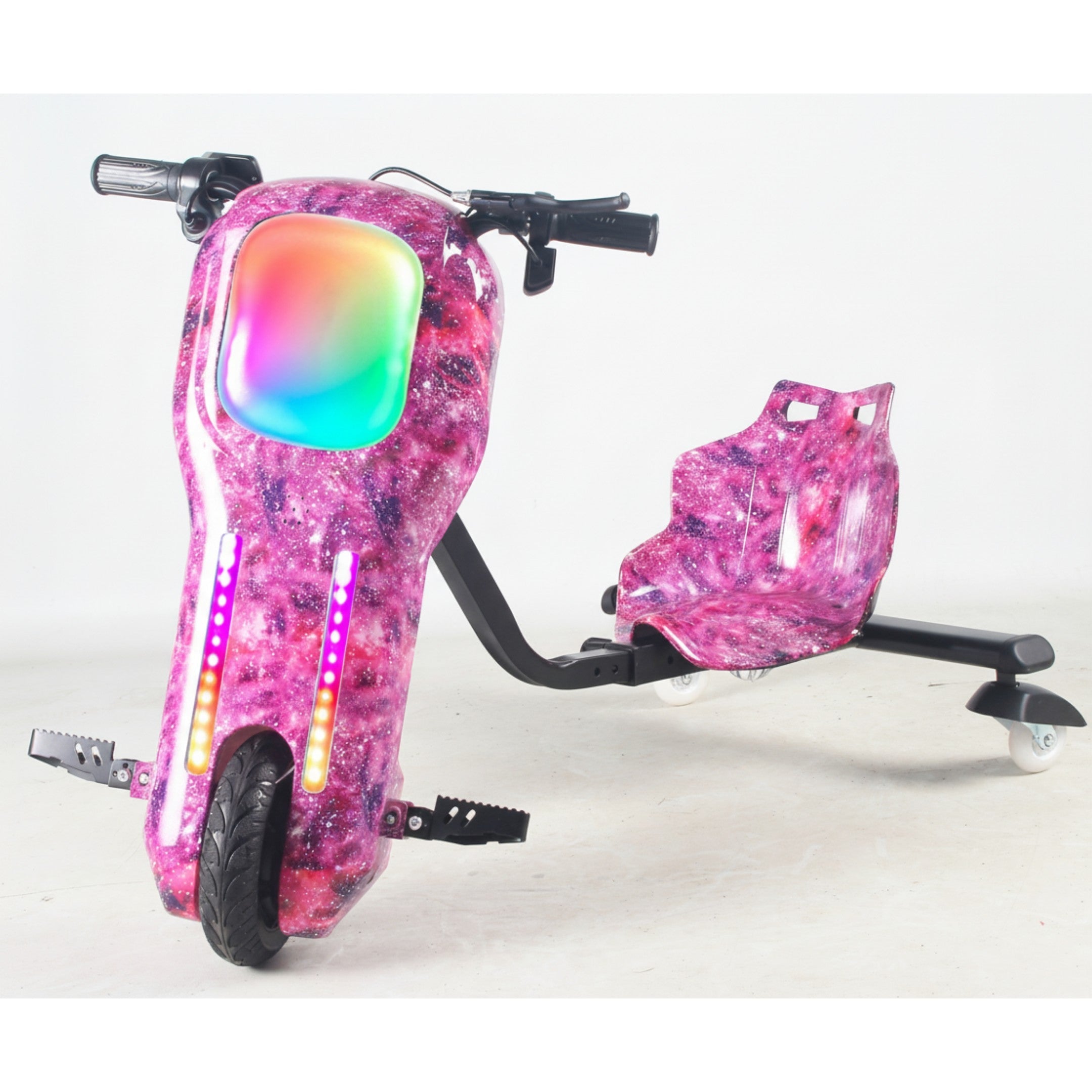 A vibrant pink and purple galaxy-patterned electric drift trike is shown from a three-quarter angle. It features a large front wheel, black foot pegs, and black handlebars. The front body displays a glowing rainbow-colored light panel and two vertical strips of individual pink, orange, and yellow LED lights. A matching galaxy-patterned bucket seat is attached to a black frame at the rear, supported by two small white wheels. The product rests on a light gray studio floor against a plain white background.